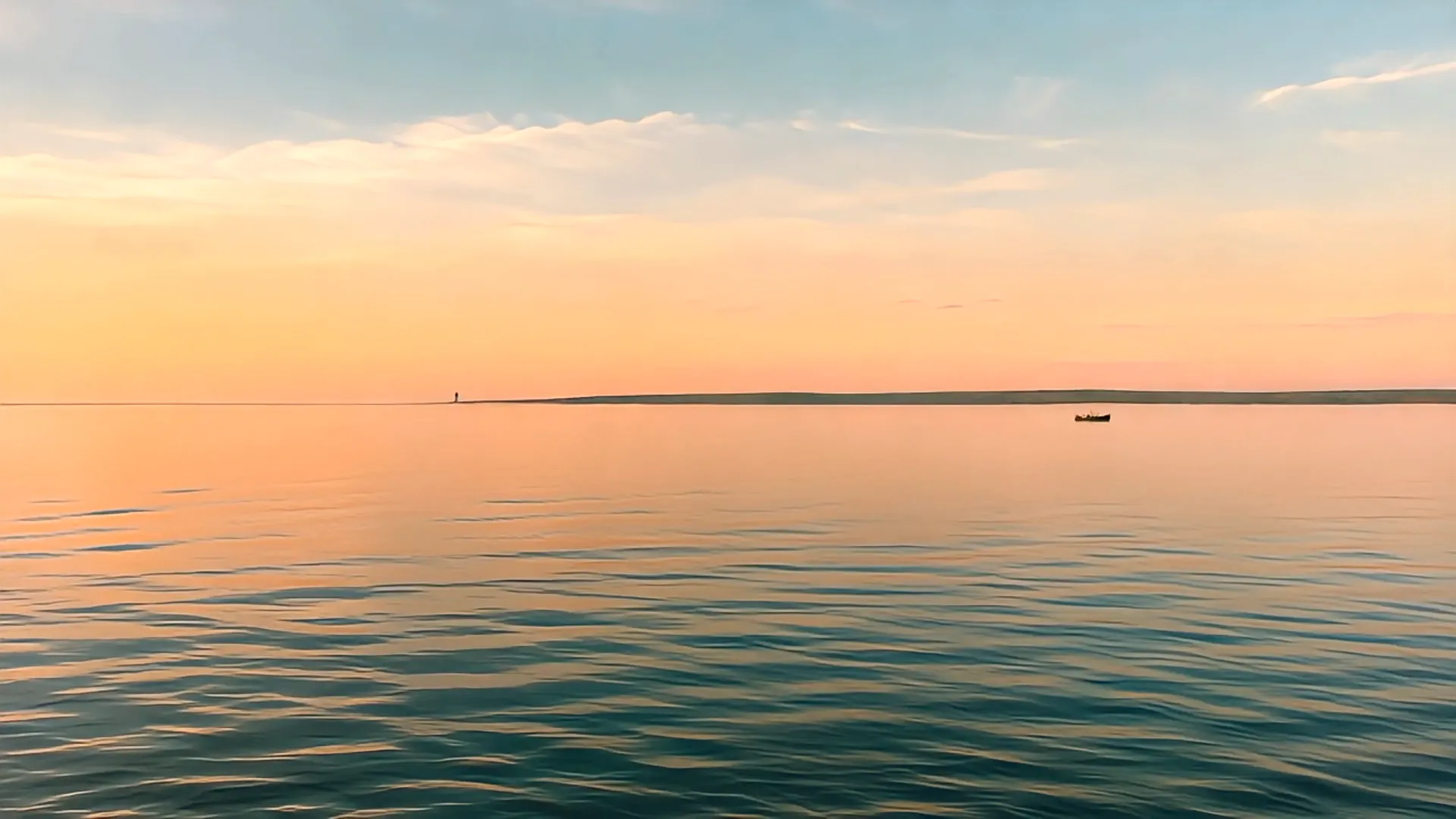 Cape Cod at golden hour: calm water, a distant lighthouse, a small boat near the horizon.